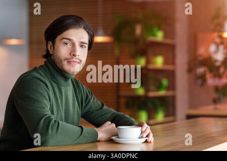 Young handsome man sitting alone at cafe, drinking coffee Stock Photo