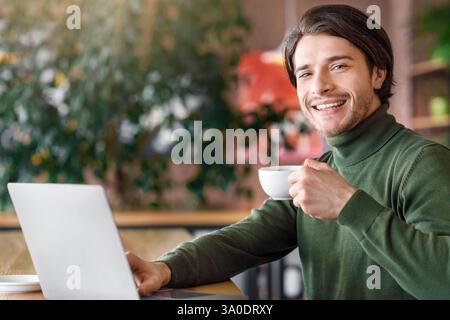 Positive freelancer working with laptop at cafe, drinking coffee Stock Photo