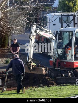 February 2025 - Men leaning on their shovels watching a small digger at work Stock Photo