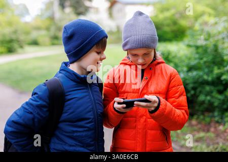 Portrait two happy smiling friends boys enjoy watching shorts video on social media at smartphone. Children enjoy playing game together sharing phone Stock Photo