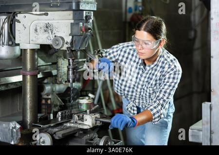 Young woman working on drilling machine in metalworking workshop Stock Photo