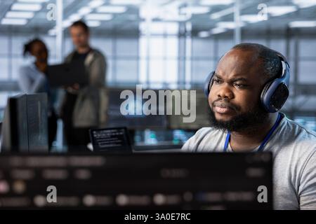 Admin in server hub listening music and ensuring compliance with industry standards and regulatory requirements. Data center worker wearing headphones enjoying songs and conducting security audits Stock Photo