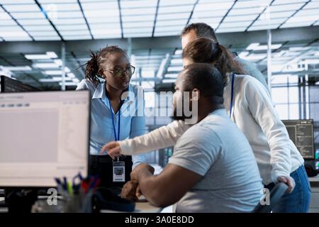 System admins doing brainstorming in computer network security data center workplace, ensuring optimal performance. Coworkers monitoring energy consumption across server racks, working together Stock Photo