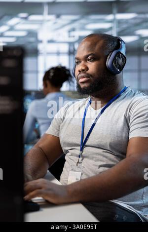 Technician listening music, using machine learning applications to optimize server farm operations. IT expert waring headphones hearing podcast while implementing server virtualization in data center Stock Photo