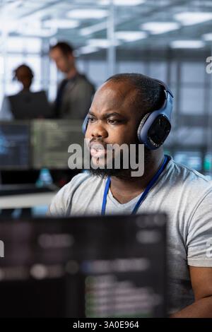 Engineer in data center listening music, optimizing IT infrastructure using network management skills. Server room expert wearing headphones upgrading gear, reducing operational costs Stock Photo