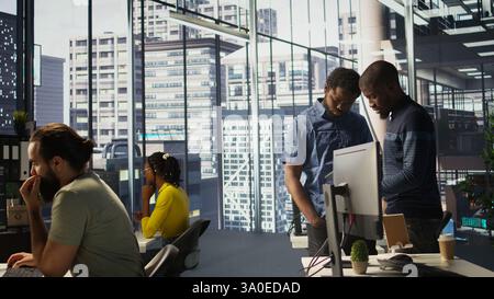 Technician and colleague using device for managing cloud computing platforms training machine learning models. IT staff members in office monitoring company systems using tablet, camera B Stock Photo