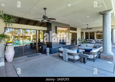 Outdoor patio and lounge area with television and fireplace with a swimming pool reflected in the glass door in a large estate in Indian Wells, Califo Stock Photo