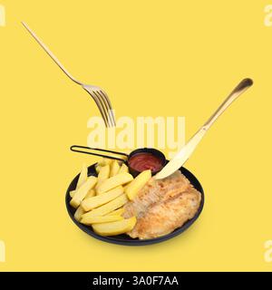 Cutlery in air over plate with delicious fish and chips on pastel yellow background Stock Photo