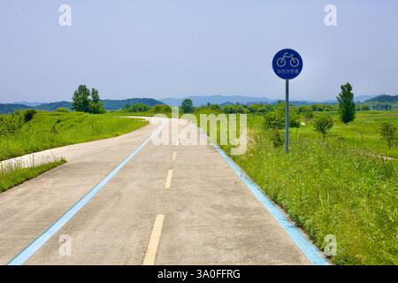 Buyeo County, South Korea - May 27, 2021: A winding dedicated bicycle path stretches through lush green fields under a clear sky, marked with a blue-l Stock Photo