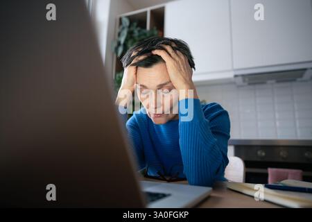 Burnout woman. Fatigued female slumped near laptop, battling eye strain from prolonged screen use Stock Photo