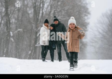 Girl is standing in front of his parents and brother. Happy family is outdoors, enjoying snow time at winter together. Stock Photo