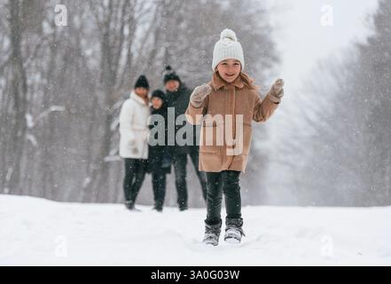 Girl is standing in front of his parents and brother. Happy family is outdoors, enjoying snow time at winter together. Stock Photo