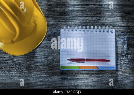 Checked notepad pen hard hat on wooden board Stock Photo