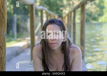 Close-up of a beautiful brunette woman in swimsuit lying on a wooden pontoon on a lake looking at the camera Stock Photo