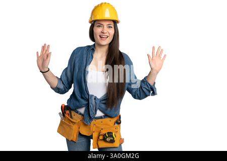 A cheerful female construction worker wearing a yellow hard hat and denim shirt raises both hands in an enthusiastic gesture. Her friendly and energet Stock Photo