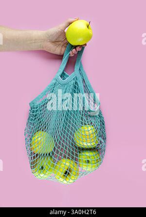A person is holding a green mesh bag with a yellow apples in it. Concept of freshness and health. Vertical crop. Stock Photo