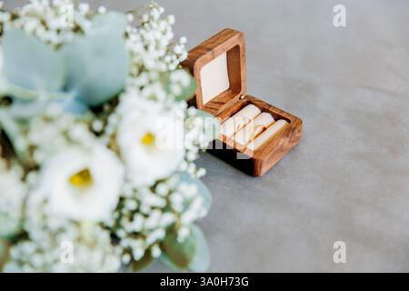 Close up of an open wooden weeding ring box with golden rings and a bride bouquet Stock Photo