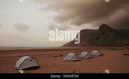 Tent shelters are set up along the beach in Socotra as dark clouds gather in the sky during twilight. Stock Photo
