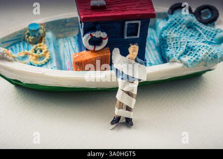Tiny wrapped figurine of man model beside a model boat Stock Photo