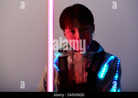 A stylish young Asian man in a futuristic outfit shines under neon lights. Stock Photo