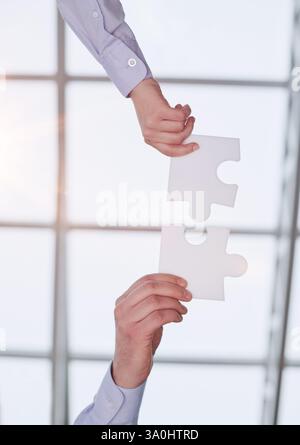 Putting the pieces together. an unidentifiable businesswoman holding two puzzle pieces together in the office. Stock Photo