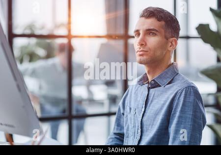 A young pensive man works in the office and thinks about something. Stock Photo