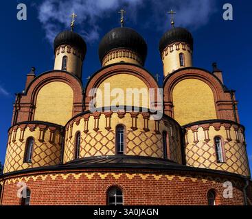 A striking view of a historic church with three domes, featuring a mix of yellow and red brick patterns. The sky is clear and blue, enhancing the arch Stock Photo