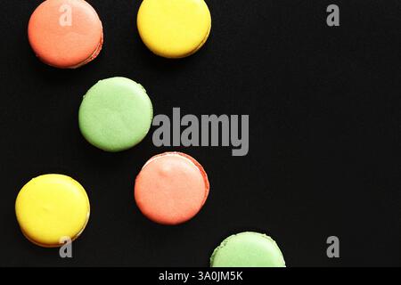 Bright French macarons on a black background, top view. Assortment of multi-colored macarons with different flavors. Delicious pastries, flat lay. Foo Stock Photo