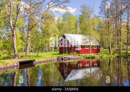 Red barn by a water pond with reflections in the water in spring Stock Photo
