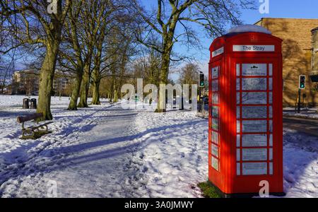 In a scene in a snowy park, a red telephone box converted as an information booth serves as a focal point, Harrogate, UK. Stock Photo