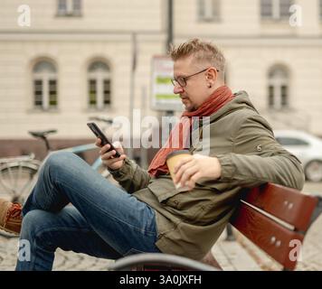 Stylish Man On City Bench Drinking Coffee Browsing Internet Stock Photo