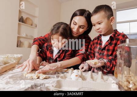 Happy mother and children baking together, family fun in the kitchen, messy hands, playful bonding, homemade cooking, joyful childhood moments. Stock Photo