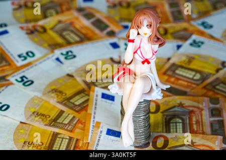 A young woman doll figurine in a swimsuit sits on a pile of coins on a background of euro banknotes Stock Photo