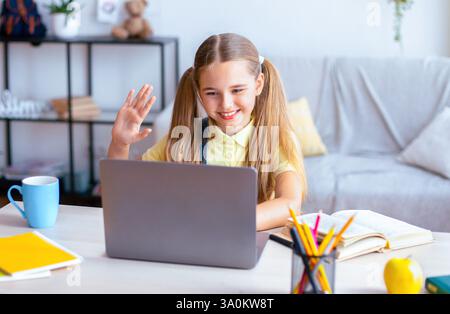 Girl sitting at desk, using laptop and waving at camera Stock Photo