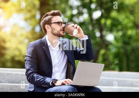 Corporate employee drinking coffee while using laptop on stairs at park Stock Photo