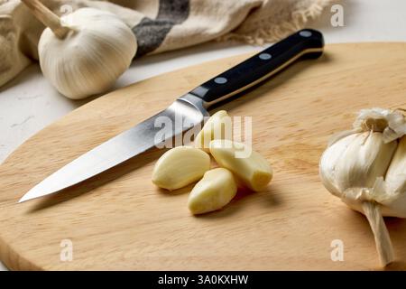 fresh raw garlic and knife on kitchen table on wooden cutting board. Process of making french onion soup, food closeup, cutting garlic for healthy mea Stock Photo