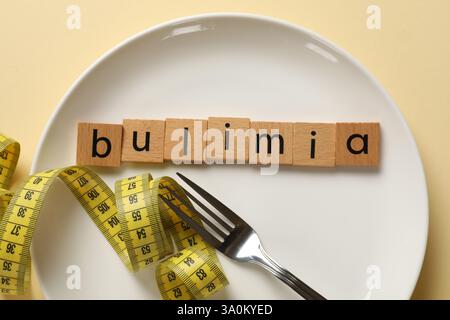 Plate with word Bulimia, fork and measuring tape on beige background, top view Stock Photo