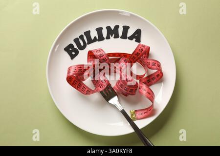 Plate with word Bulimia, measuring tape and fork on olive background, top view Stock Photo
