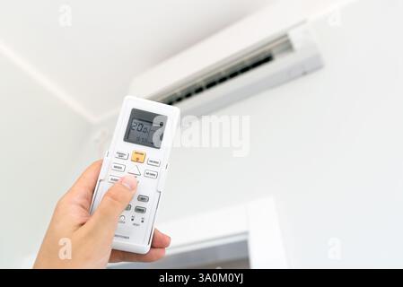 Air conditioner temperature adjustment with remote controller in room at home. Stock Photo