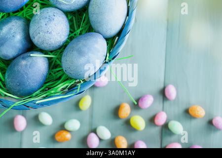 Naturally dyed blue Easter eggs in a basket with candy in background. Selective focus with blurred background. Stock Photo
