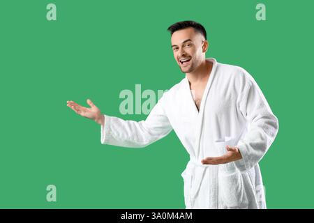 Happy young man in bathrobe showing something on green background Stock Photo
