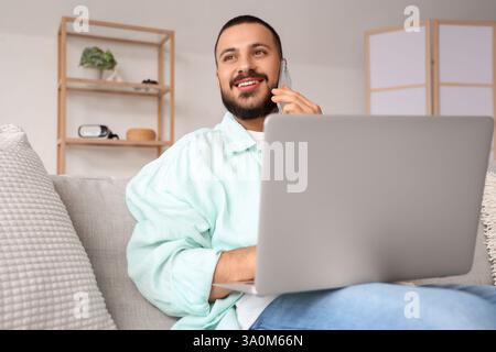 Young man working with laptop while talking on mobile phone Stock Photo