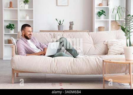 Freelancer lying on sofa and using laptop at home Stock Photo