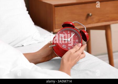 Female hands with red alarm clock on bed in bedroom Stock Photo