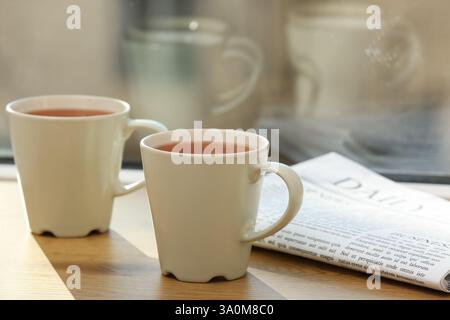 White cups of hot black tea on windowsill against window. Closeup Stock Photo
