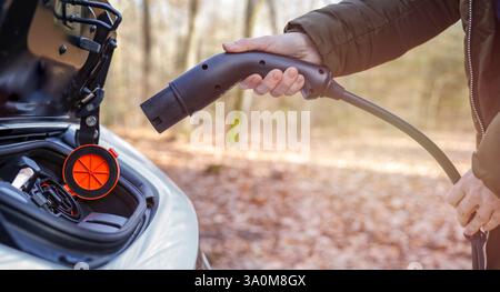 Close-up of an electric car's charging port with a hand plugging in a charging connector. Stock Photo