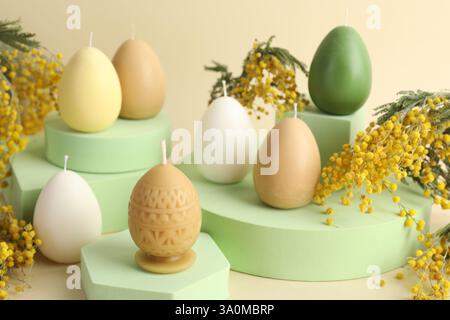 Beautiful egg shaped candles and mimosa flowers on beige background. Easter decor Stock Photo