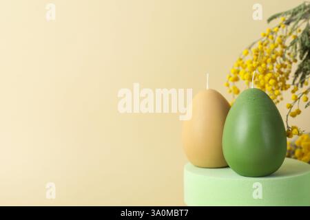 Beautiful egg shaped candles and mimosa flowers on beige background, closeup with space for text. Easter decor Stock Photo