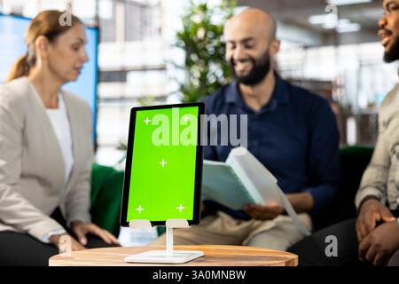 Smiling multiracial employees in office maintaining relationship with business partners, looking at metrics on green screen tablet. Upbeat diverse managers showing shareholders data on mockup device Stock Photo
