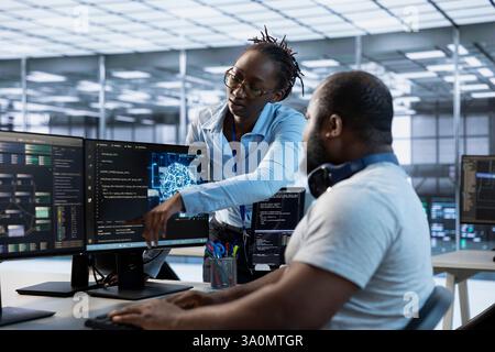 Manager showing engineer how to finish tasks in data center providing resources for different workloads. Team leader teaching IT specialist how to monitor supercomputers, pointing to screen Stock Photo